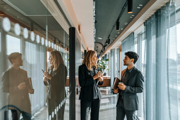 Male and female business professionals discussing with each other while standing in office corridor