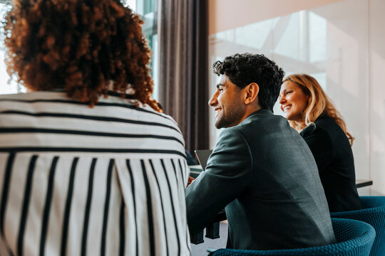 Young smiling male entrepreneur with female colleagues sitting in board room during meeting at office