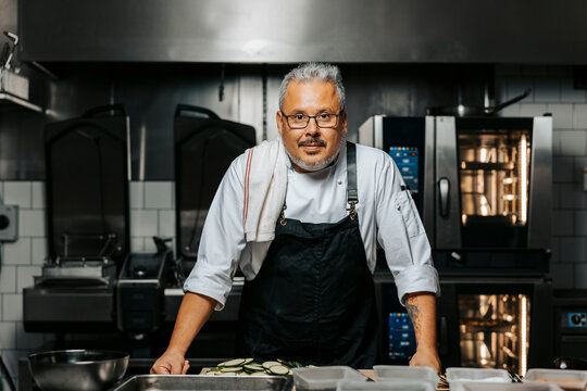 Portrait of mature male chef wearing apron and standing in kitchen at restaurant