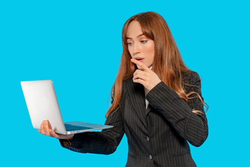 Woman in business attire looks surprised while using laptop against blue background