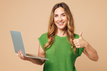 Young smiling happy IT woman she wear green t-shirt casual clothes hold use work on laptop pc...