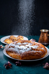 Banana Tarte Tatin is sprinkled with powdered sugar on a white plate on a dark background. The powder is poured onto the cake. Vertical Photo