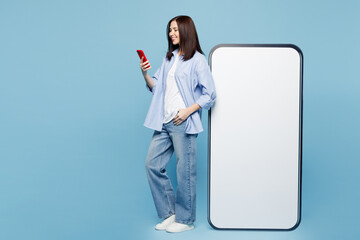Full body side profile view young Caucasian woman wears shirt casual clothes big huge blank screen mobile cell phone with area using smartphone isolated on plain pastel light blue background studio.