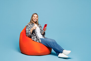 Full body young woman she wears checkered grey shirt casual clothes sit in bag chair hold in hand...