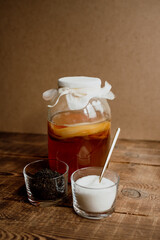 Fresh kombucha in a glass jar on a wooden background and ingredients for cooking black tea and sugar.