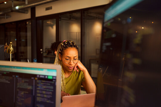 Braided hair businesswoman leaning on elbow while working on laptop in tech startup office