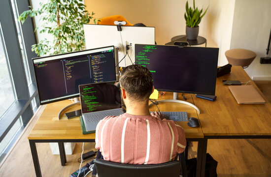 High angle rear view of male programmer coding on laptop while sitting at desk in startup office