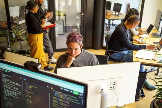 High angle view of focused non-binary computer programmer working on desktop PC in office