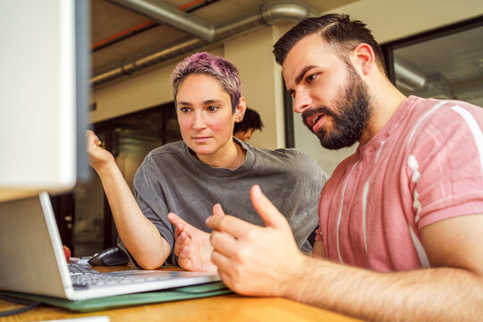 Male IT professional discussing with non-binary person in tech startup