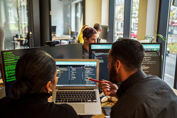 Rear view of male and female coding professional discussing over laptop while working in tech startup office