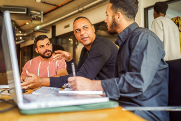 Male computer programmers discussing with each other while sitting at desk in office