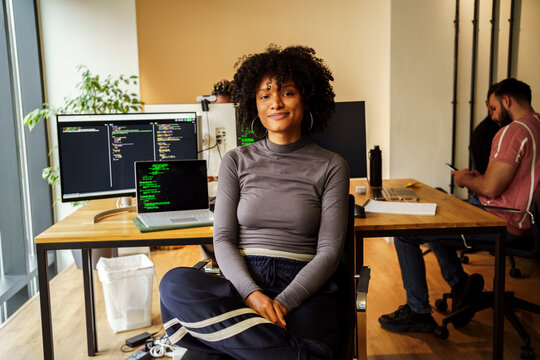Portrait of curly haired female IT professional sitting in front of desktop PC at tech office
