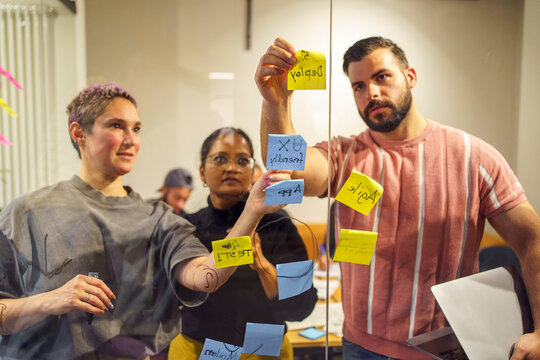 Business people sticking adhesive note on glass wall in meeting room at tech hub