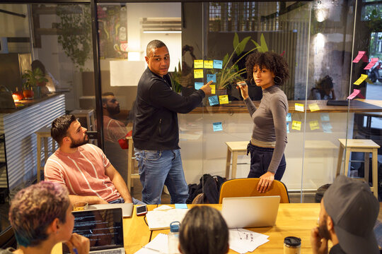 High angle view of male and female business entrepreneurs standing near glass wall and discussing with colleagues in mee