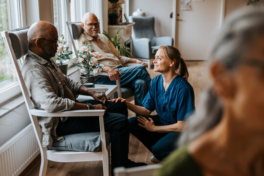 Smiling nurse talking with elderly man sitting on chair at care home - Powered by Adobe