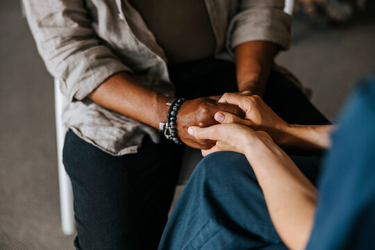 High angle view of female healthcare professional holding hands of patient during consoling session at nursing home