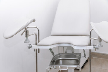 White modern gynecological examination chair for women. Medical chair in the gynecologist's office with white wall. Reproductive system and Pregnancy concept. High quality photo. Copy space