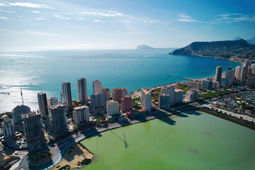 Obraz premium Aerial shot of Calpe cityscape. Costa Blanca, Spain. Coastal town with towering residential and commercial buildings lining salt lake and Mediterranean Sea shoreline. Travel and touristic places conce