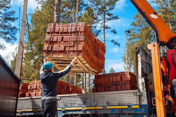 Workers unload bricks from a delivery truck using a crane in a construction area
