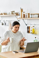 A young plus sized woman enjoys a lively conversation while sipping coffee in her kitchen.