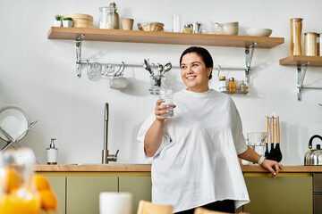 A young woman smiles in a stylish kitchen, holding a glass of refreshing water.