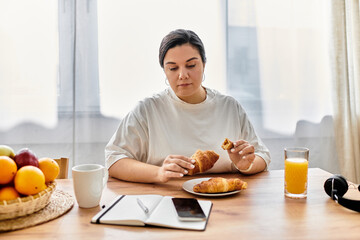 A young plus sized woman savoring a croissant at a cozy breakfast table with bright natural light.