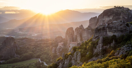 Amazing panoramic view of the Meteora valley with the monasteries in the golden hour of the sunset against the background of the setting sun, near Kastraki, Greece.