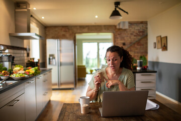 Woman having video call while drinking coffee in kitchen