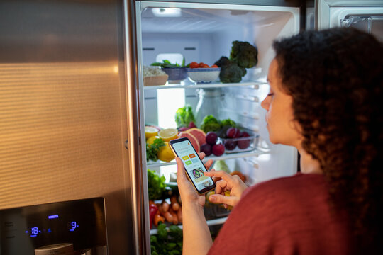 Woman using smartphone app to manage grocery inventory in smart refrigerator