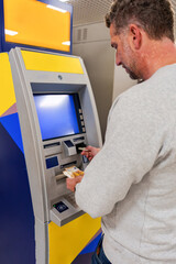 Male hand pulling cash from ATM, accessing bank funds swiftly during urban banking transaction on city street