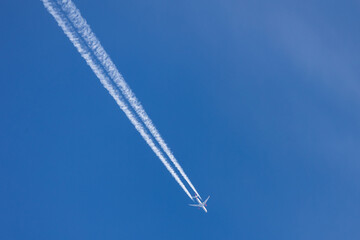 Ein Verkehrsflugzeug fliegt hoch am Himmel und hinterlässt zwei lange, weiße Kondensstreifen vor...