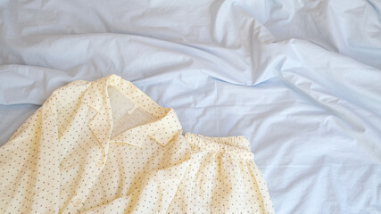 Close-up of pajamas lying on a bed with pastel blue bed linen. Сopy space. Concept of soft, cozy, relaxing sleep atmosphere.