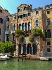 A beautiful Venetian building situated right on the water's edge. The building's intricate details, including arched windows and balconies adorned with flowers, give it a classic Venetian charm.