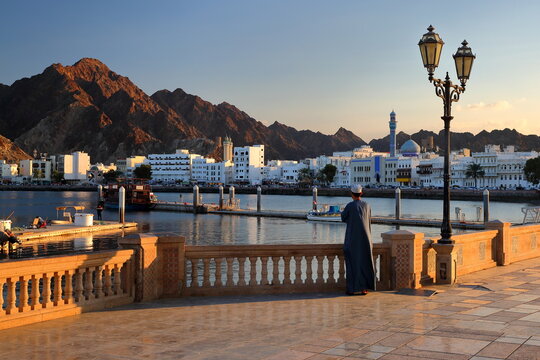 The Muttrah corniche viewed from the esplanade next to the fish market at sunset, with an Omani man traditionally dressed and the mosque and mountains in the background, Muttrah, Muscat, Oman