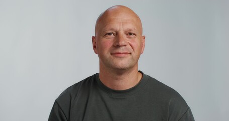Fototapeta premium A bald man puts patches under his eyes. He smiles at the camera while standing in the studio background