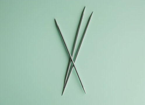 Three Silver Knitting Needles on a Mint Green Background