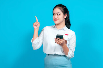 Naklejka premium Smiling female student dressed in a uniform pointing while holding a smartphone
