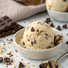 A bowl of ice cream with chocolate chips and brownie pieces, surrounded by chocolate pieces and brownie crumbs
