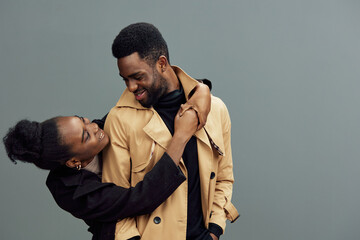 Young African couple sharing a joyful moment, dressed in trendy clothing, set against a neutral gray background, infusing warmth and love into the scene