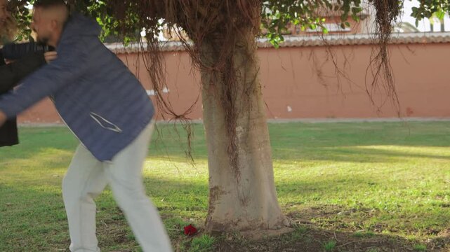 Romantic couple sharing intimate moment, holding each other tenderly under lush green tree branches, expressing deep emotional connection.