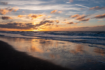Obraz premium A beautiful sunset casts colorful hues on ocean waves, reflecting brilliantly on the wet beach sand