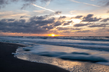 A breathtaking sunset paints the vibrant sky while gentle ocean waves softly lap against the sandy...