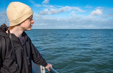 A young man gazes thoughtfully at the tranquil ocean, beautifully framed by a vibrant, colorful sky above him