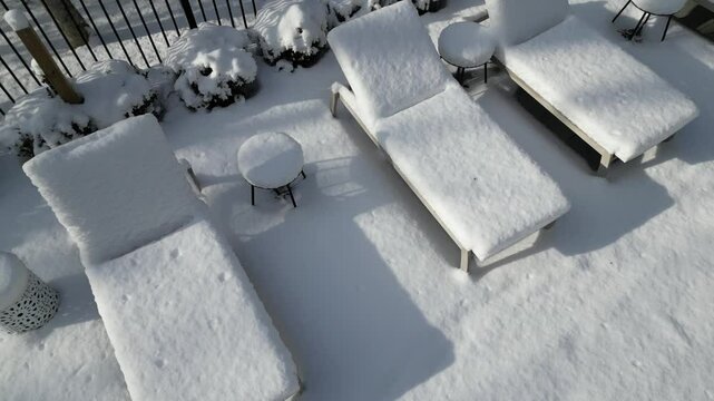 aerial view of snow covered lounge chairs next to closed shuttered swimming pool in winter (back yard patio loungers outdoor furniture) spa bizzard snowy snowfall frozen home countryside drone footage