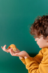 Curly cheerful shaggy shaggy boy with glasses holding orange eublepharis on green background. Concept of unusual pets that are safe for allergic children. 