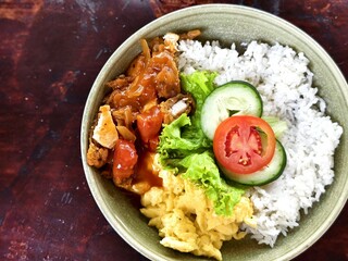 Rice bowl with scrambled eggs, fried sliced chicken, teriyaki sauce, lettuce, cucumber, and tomato slices
