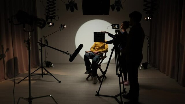 Studio for photo video production with lighting equipment and cyclorama, model actor sits on director chair in the middle and recording interview.
