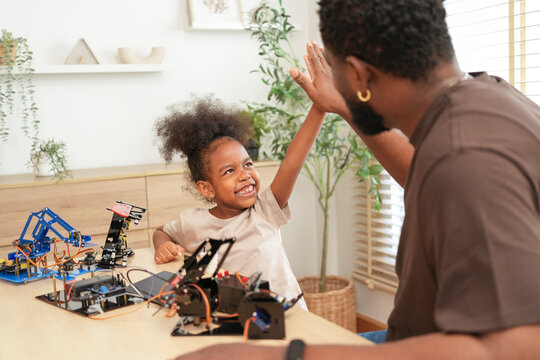 Excited father and daughter giving a high five after successfully assembling a robotics project, enjoying a fun and educational STEM activity that fosters teamwork and creativity at home