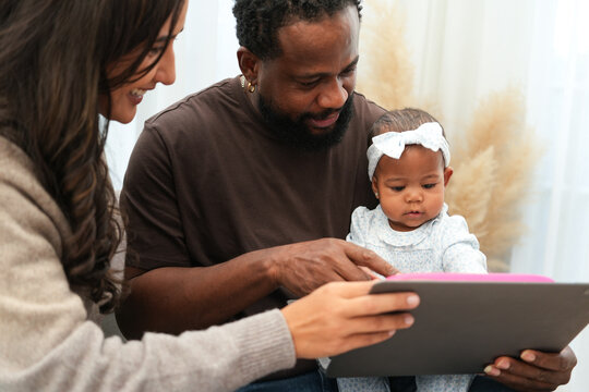 Loving mother and father sitting on a cozy couch, joyfully interacting with their baby while using a tablet, creating a warm and happy family bonding moment at home