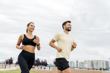 Young couple enjoys jogging together in a city park under a cloudy sky in the afternoon